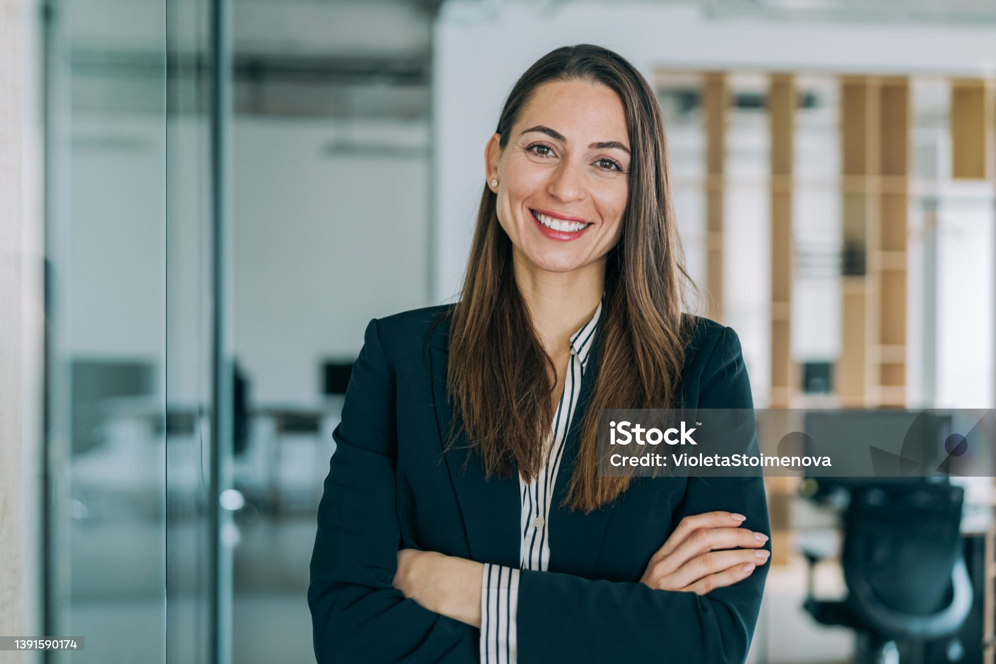 Portrait of a beautiful smiling businesswoman standing with crossed arms in her office and looking at camera.